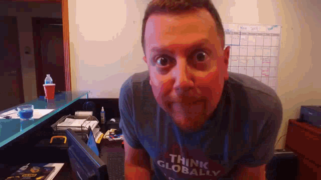a man wearing a shirt that says think globally looks at the camera