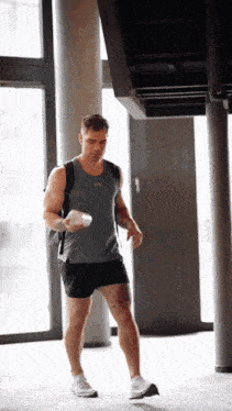 a man wearing a grey under armour tank top and black shorts is walking