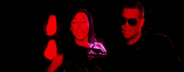 a man and a woman are in a dark room with red lights behind them