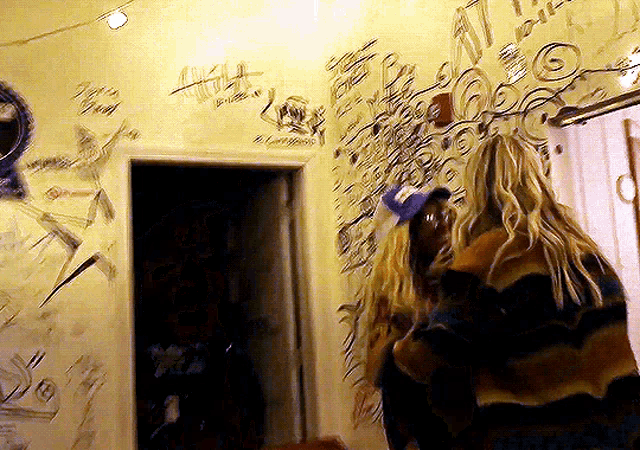 a woman in a striped sweater stands in front of a wall with drawings on it
