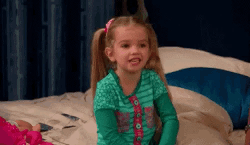 a little girl is sitting on a bed with a doll .