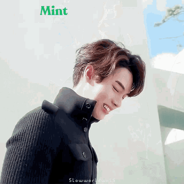 a man wearing a black sweater is smiling in front of a mint sign