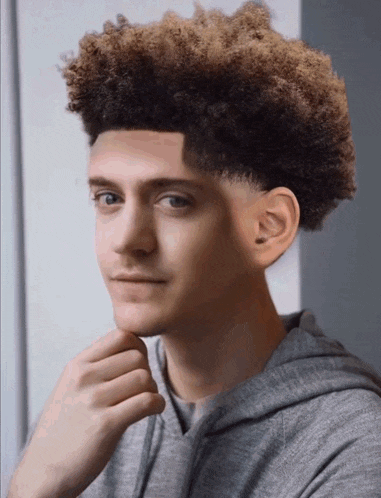 a young man with curly hair and a gray hoodie