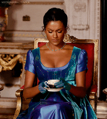a woman in a blue dress sits in a chair holding a cup