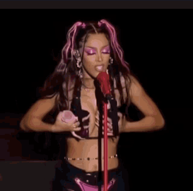 a woman with pink hair is singing into a microphone while wearing a crop top .