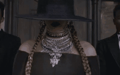 a woman wearing a hat and a necklace is standing in front of a group of men .