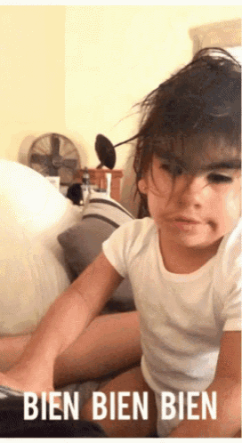 a little girl in a white shirt is sitting on a bed with the words bien bien beneath her