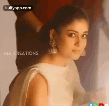 a woman wearing a white dress and earrings is looking at the camera .