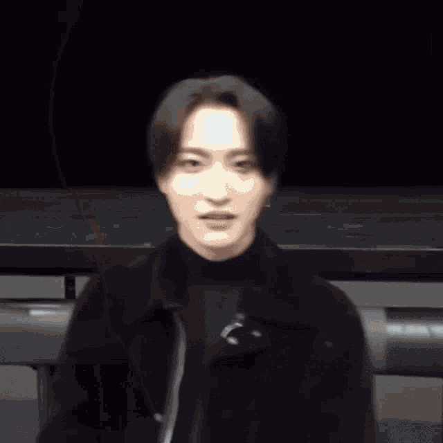 a man in a black jacket is standing in front of a black background .