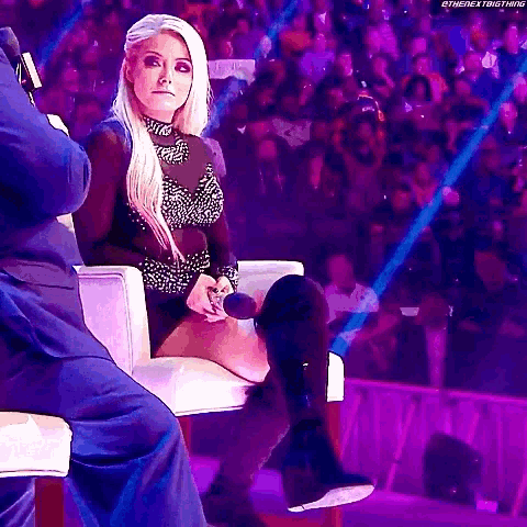 a woman is sitting in a chair in front of a crowd with a microphone in her hand .