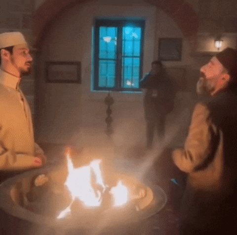 two men are standing around a fire in a dark room .