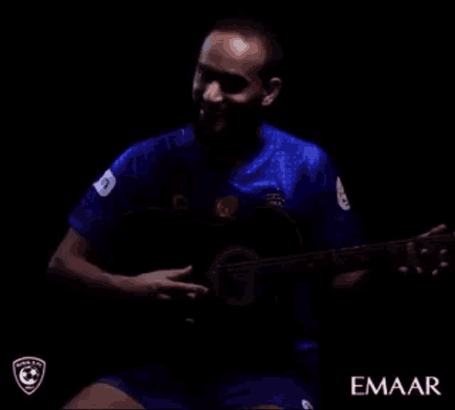 a man in a blue shirt is playing a guitar and the word emaar is on the bottom