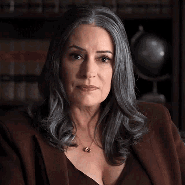 a woman with gray hair wearing a necklace and a brown jacket