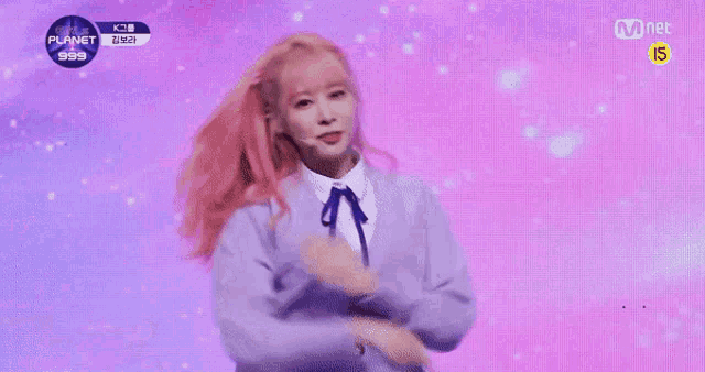 a girl with pink hair is standing on a stage wearing a purple sweater and a blue bow tie .