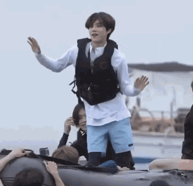 a man wearing a life jacket is standing on top of a boat with other people .