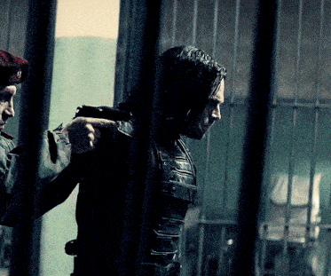 a man in a beret holds a gun to another man behind bars