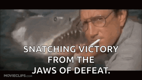 a man with glasses is smoking a cigarette in front of a shark and the words snatching victory from the jaws of defeat