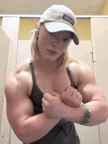 a woman wearing a patagonia hat flexes her muscles in a bathroom