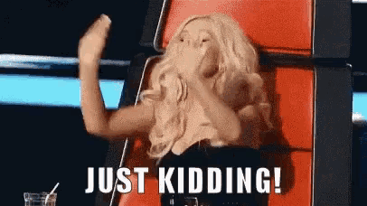 a woman is sitting in a red chair and covering her mouth with her hands and the words just kidding !