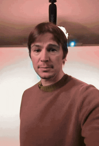 a man in a brown sweater stands in front of a rode microphone