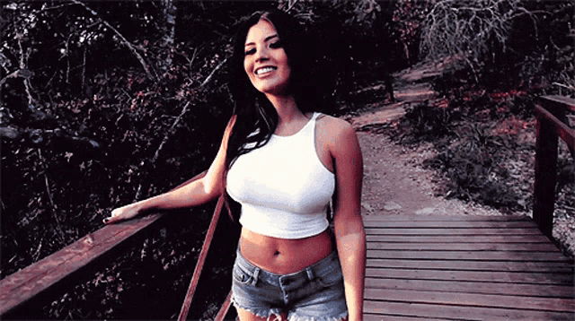 a woman in a white tank top and shorts stands on a wooden deck