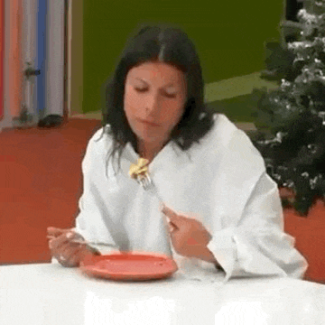 a woman in a white shirt is sitting at a table eating food with a fork and knife .