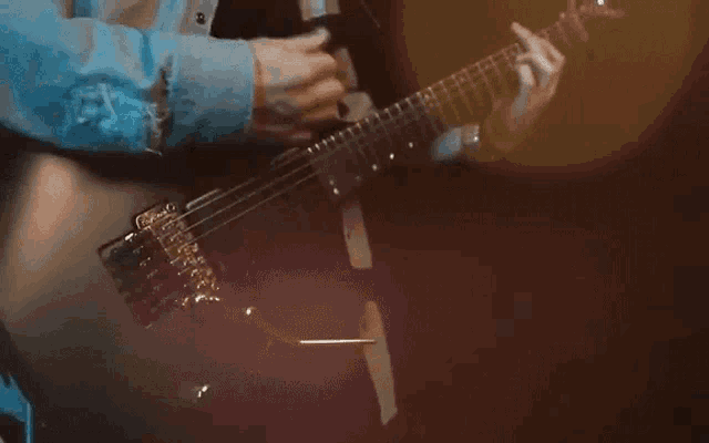 a man in a denim shirt is playing a black electric guitar