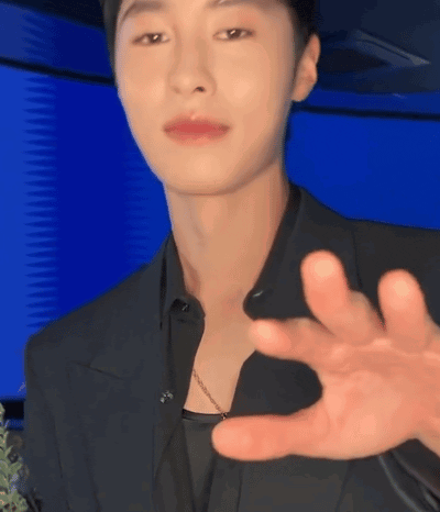 a man in a black suit is making a gesture with his hands