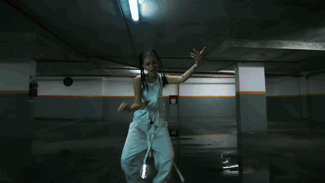 a woman in a white tank top stands in a dark room