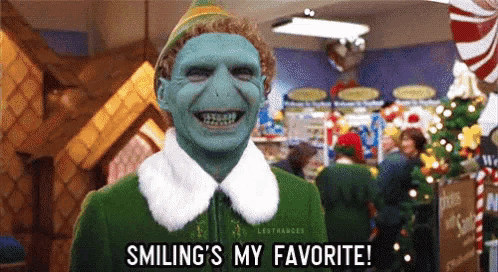 a christmas elf with a blue face is smiling and says smiling 's my favorite .