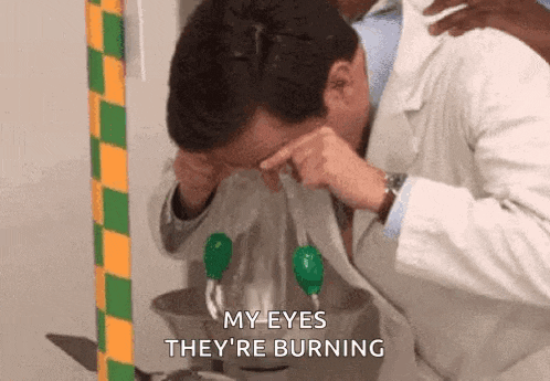a man in a lab coat is washing his eyes in a bathroom .