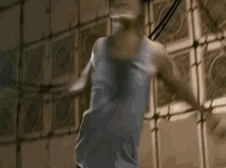 a man in a tank top is standing in front of a wall with a lot of pictures on it .