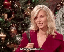 a woman in a red coat is standing in front of a christmas tree .