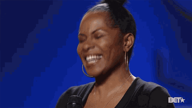a woman is laughing in front of a blue background that says bet