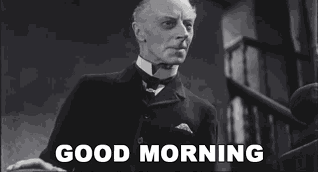 a man in a suit and tie is standing in front of stairs and says good morning .
