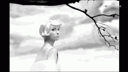 a black and white photo of a woman standing under a tree branch .