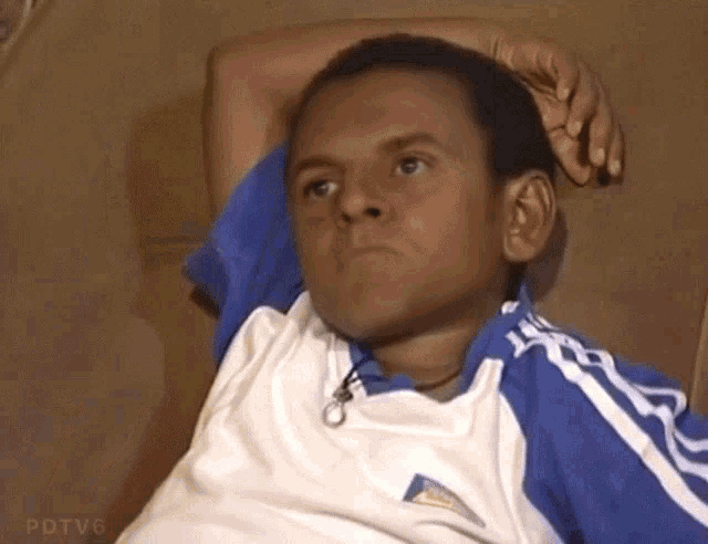 a man in a blue and white adidas shirt is sitting on a couch with his hand on his head
