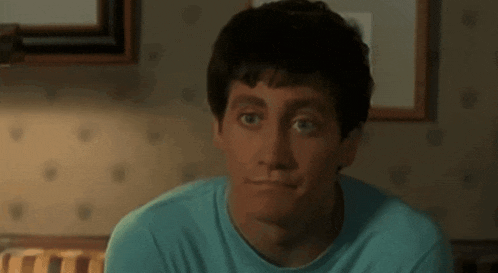 a man in a blue shirt is sitting on a bed looking at the camera .
