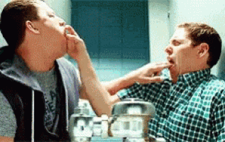 two men are touching each other 's faces in front of a bathroom mirror .