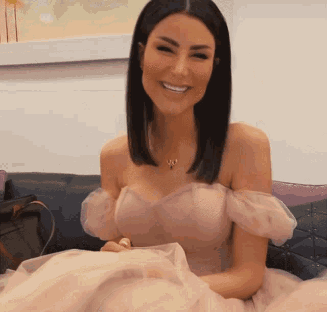 a woman in a pink dress is sitting on a couch and smiling