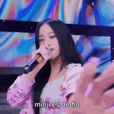 a girl is singing into a microphone with the words minji es de flo written below her
