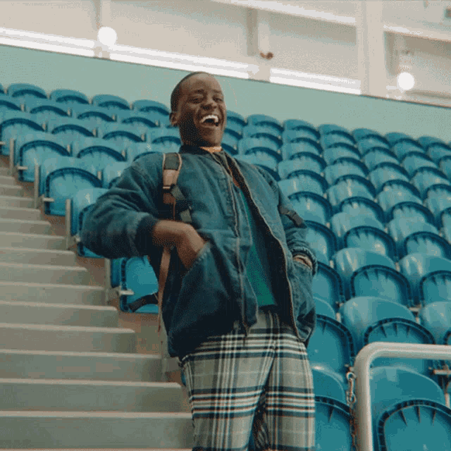 a man wearing plaid pants and a denim jacket stands on a set of stairs