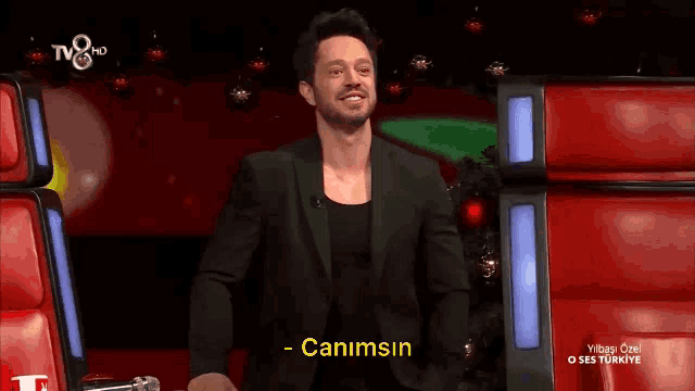 a man in a black suit stands in front of a microphone and says " canimsin " on the screen
