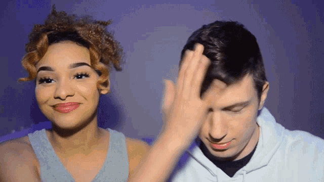 a man and a woman are standing next to each other and the woman is touching the man 's hair
