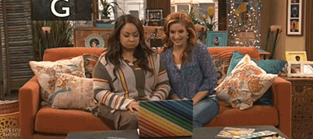 two women are sitting on a couch using a laptop .