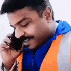 a man with a mustache is wearing a safety vest and talking on a cell phone .