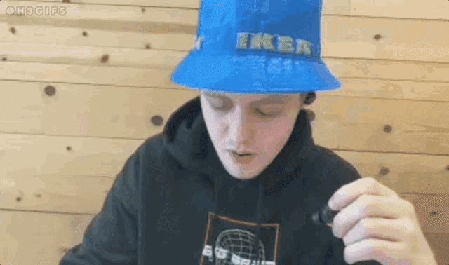 a man wearing a blue bucket hat and a black hoodie is eating a sandwich .