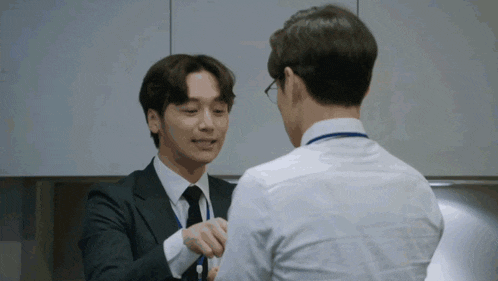 two men in suits and ties are shaking hands in a kitchen .