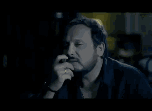 a man with a beard is smoking a cigarette in a dark room in front of a lamp .