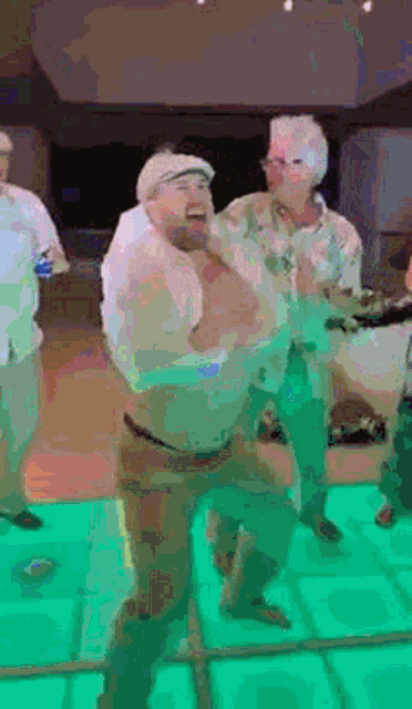 a group of men are dancing on a green dance floor